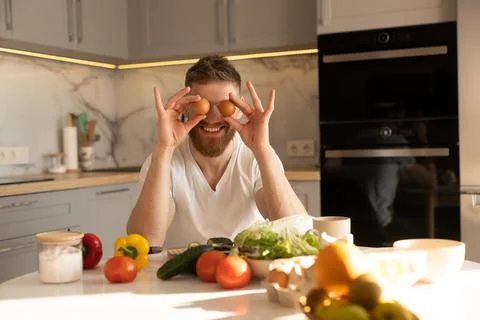 Young man joking with eggs while sitting at table Stock Photos