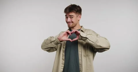 Young man joyfully expresses love with creative hand gestures in a bright s.. Stock-Footage 329112876