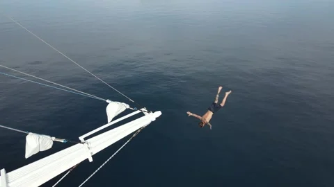 Young man jumping off cliff into blue water ocean Stock Footage 237735174