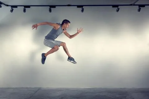 Young man jumping in front of gray wall Stock Photos