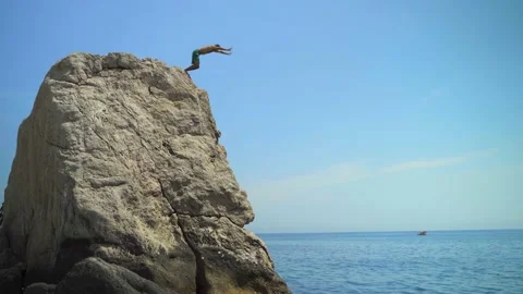 A young man jumping from a high cliff into the sea doing a forward somersault on Stock Footage 157501295