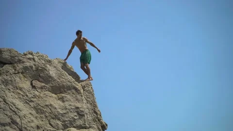A young man jumping from a high cliff into the sea doing a back somersault on a Stock Footage 157501408