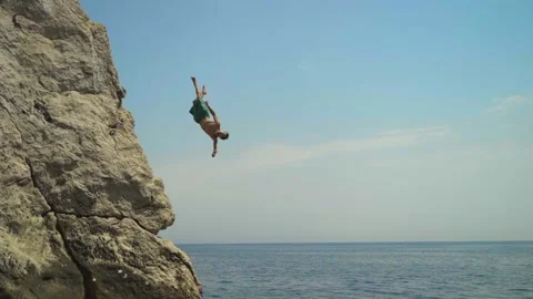A young man jumping from a high cliff into the sea doing a back somersault in Stock Footage 157502349
