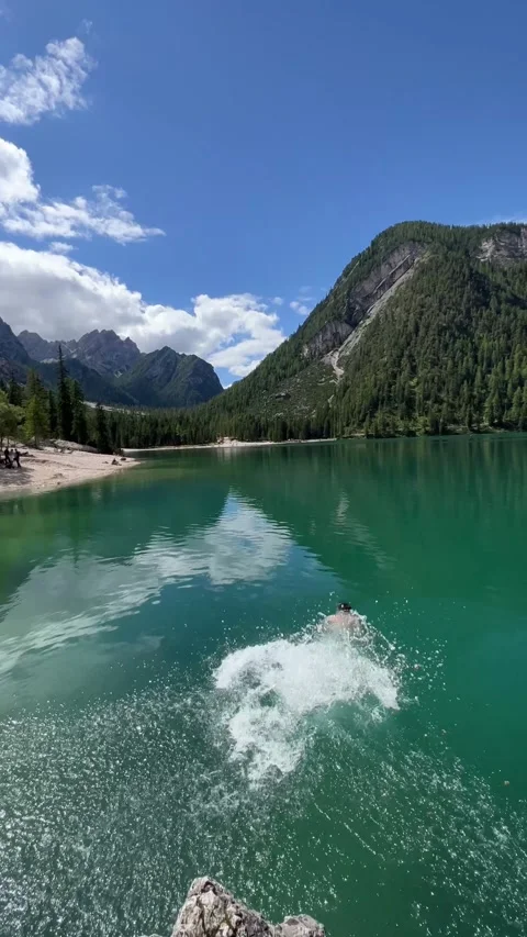 Young man jumping from a stone rock water of Italian Lago di Braies Dolomites 스톡 동영상 297868947