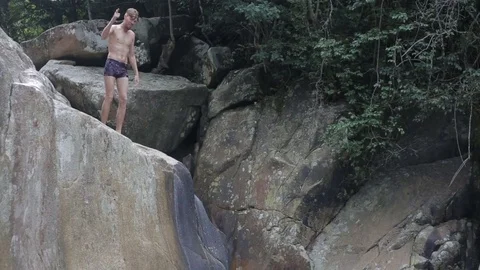 Young man jumping from waterfall rocks in the water Stock Footage 70757740