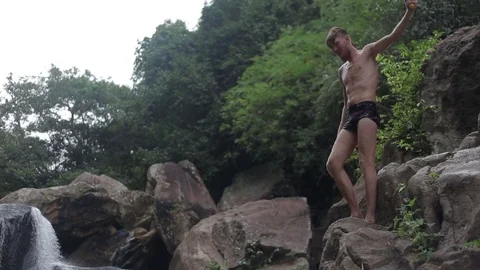 Young man jumping from waterfall rocks in the water Stock Footage 70757796