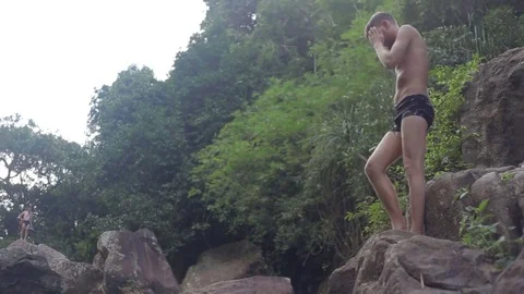 Young man jumping from waterfall rocks in the water Stock Footage 70758570