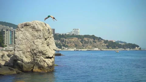 A young man jumps from a high cliff into the sea making beautiful turns in the Stock Footage 157501550