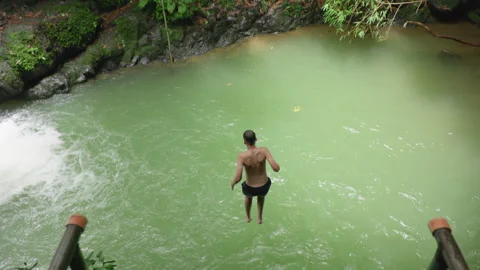 Young Man Jumps Off Platform into Tropical River Pool in Slow Motion. Stock Footage 338364600