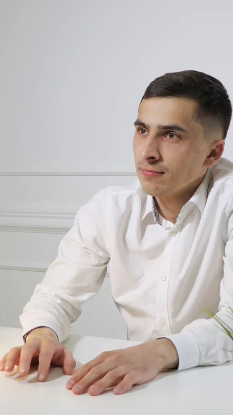 Young man keeps both hands on desk, shifting fingertips while looking forward 動画素材 346392220