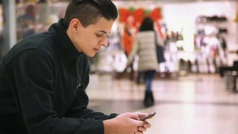 Young man keeps a smartphone and touches its screen in a modern mall Stock Footage 88227067