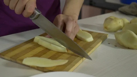 Young man in the kitchen cutting the potatoes with a knife on cutting board at Stock Footage 89600701
