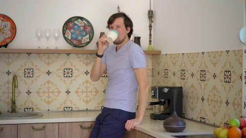 A young man in a kitchen drinks coffee. An aroma diffusor is standing on a table Stock Footage 210070038