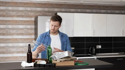 Young man in kitchen during quarantine. Recycling process. Guy sorting glass Stock Footage 128935469