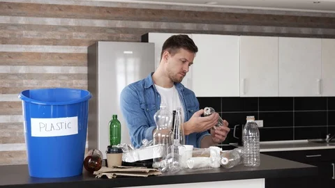 Young man in kitchen during quarantine. Sorting plastic bottle separated from Stock Footage 128935637