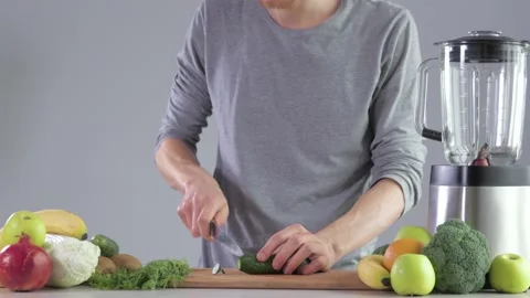A young man at the kitchen table in the kitchen cuts an cucumber for a smoothie Stock Footage 149527211