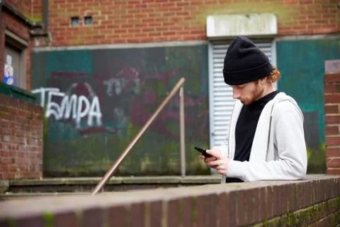 Young man in knit hat using smartphone in an urban setting Stock Photos