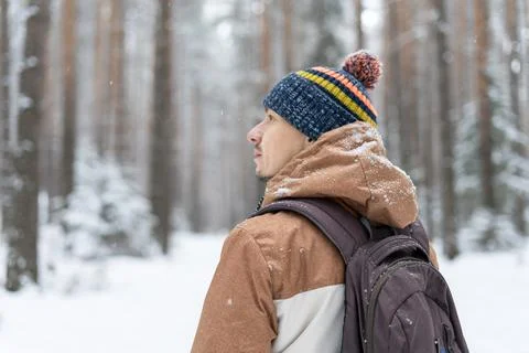 Young man in knitted hat with backpack walking in snowy forest in winter Stock Photos