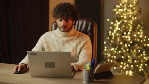 Young man in knitted sweater is working on Christmas holidays. Indoor footage Stock Footage 231568944