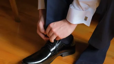 Young man lacing black leather dress shoes indoors on wooden floor Stock-Footage 342128372