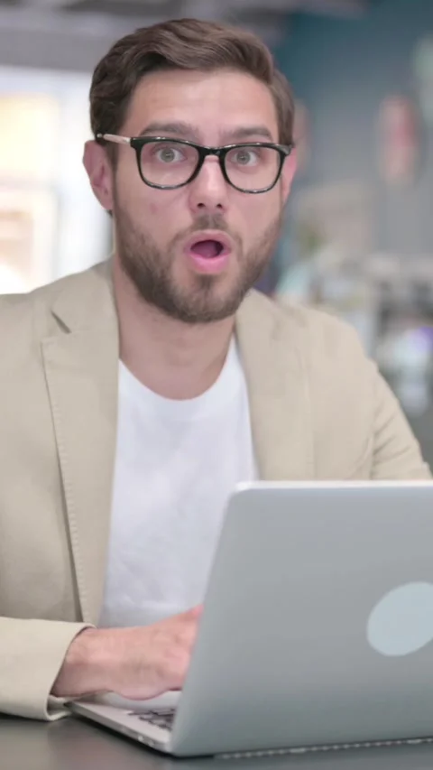 Young Man with Laptop Feeling Shocked at Work, Vertical Video Stock Footage 342003974