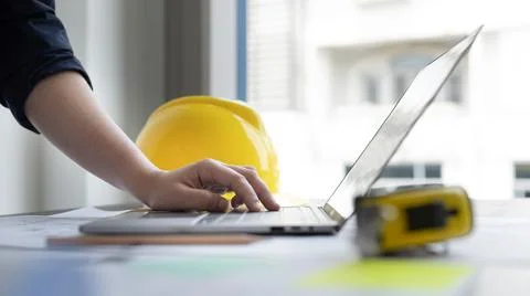 Young man with a laptop plotting a system of building structures in blueprint Stock Photos