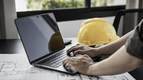 Young man with a laptop plotting a system of building structures in blueprint Stock Photos