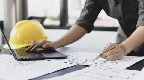 Young man with a laptop plotting a system of building structures in blueprint Stock Photos