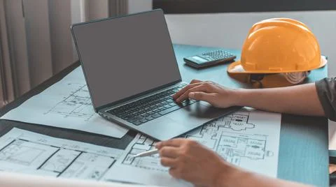 Young man with a laptop plotting a system of building structures in blueprint Fotos de archivo