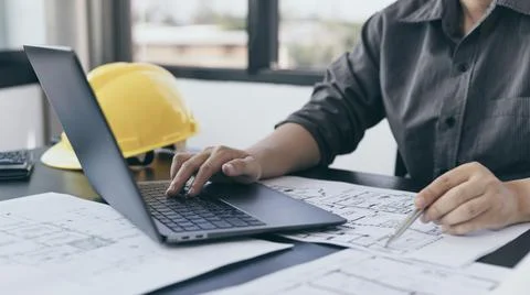 Young man with a laptop plotting a system of building structures in blueprint Fotos de archivo