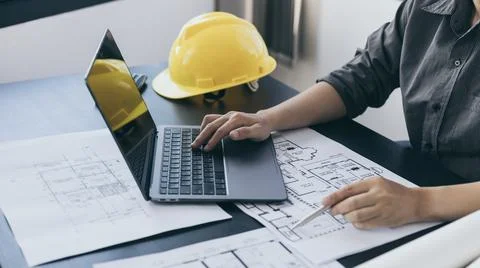 Young man with a laptop plotting a system of building structures in blueprint Fotos de archivo