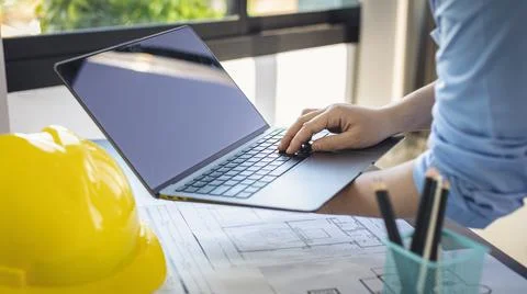 Young man with a laptop plotting a system of building structures in blueprint Fotos de archivo