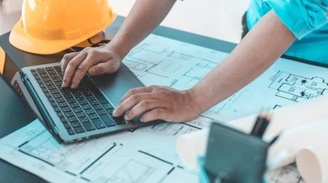 Young man with a laptop plotting a system of building structures in blueprint Stock Photos