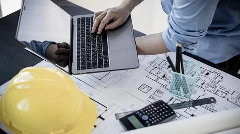 Young man with a laptop plotting a system of building structures in blueprint Fotos de archivo