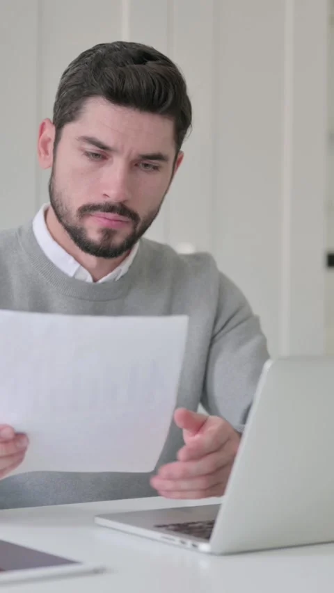 Young Man with Laptop Reading Documents in Office, Vertical Video Stock Footage 339582149