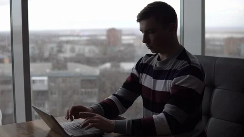A young man with a laptop sits at a table. A man sits in a cafe by the panoramic Stock Footage 127252384