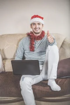 Young man with laptop on a sofa. Businessman with Santa hat Stock Photos