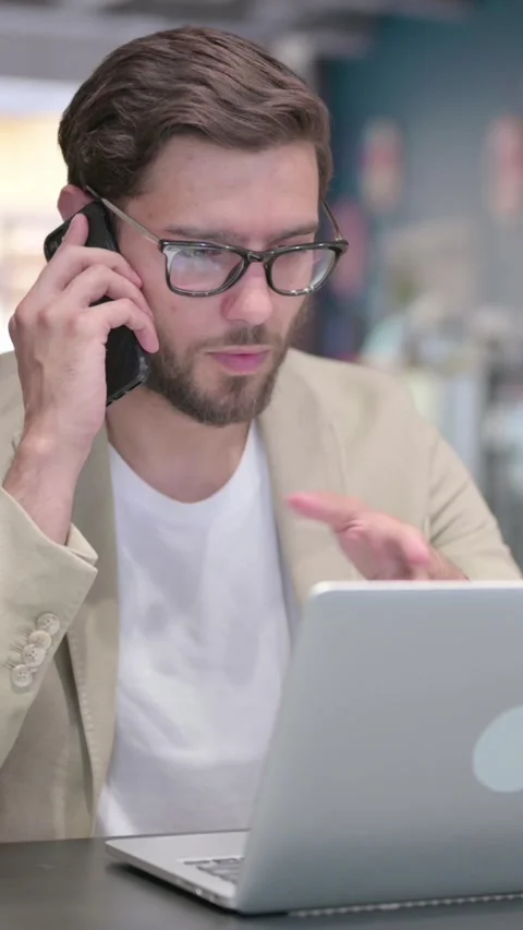 Young Man with Laptop Talking on Smartphone, Vertical Video Stock Footage 342004258