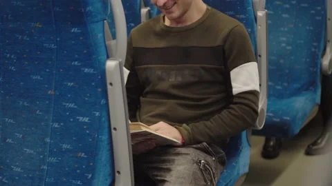 A young man laughs while reading a book on the train. winter landscapes are Stock Footage 199520039
