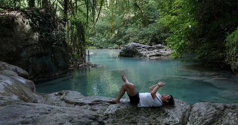 Young man laying down on a stone in the forest while watching smartphone Stock Footage 112624667