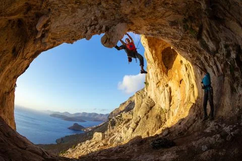 Young man lead climbing on ceiling in cave, another belaying Stock Photos