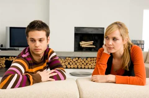 Young man leaning on a couch with a young woman looking at him Stock Photos
