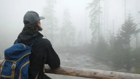 Young man leaning on the railing of an old wooden bridge, surrounded by fog Stock Footage 159674249