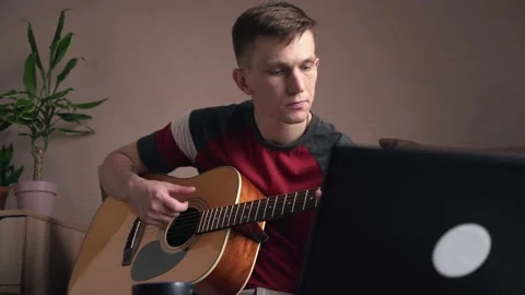 Young man is learn.ing to play the acoustic guitar. online learning. Видео 207784297