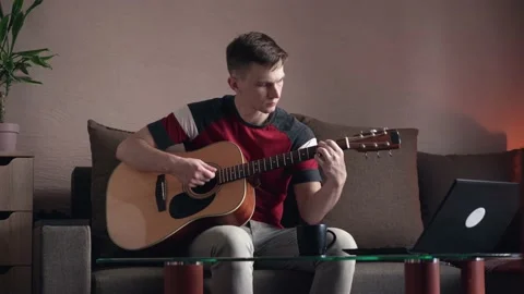 Young man learning to play acoustic guitar online at home Stock Footage 207784496