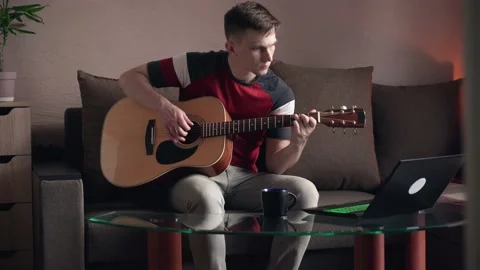 Young man learning to play acoustic guitar online at home Видео 208882057