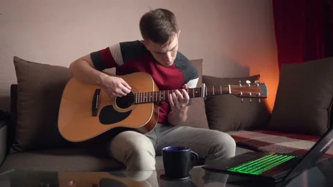 Young man learning to play acoustic guitar online at home Stock Footage 209308809