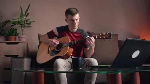 Young man learning to play acoustic guitar online at home Stock Footage 210553858