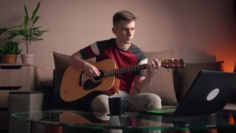 Young man learning to play acoustic guitar online at home Stock Footage 210554308