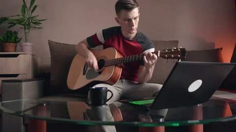 Young man learning to play acoustic guitar online at home Stock Footage 211813075